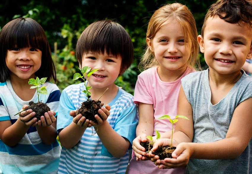 kids stand together holding plants in dirt