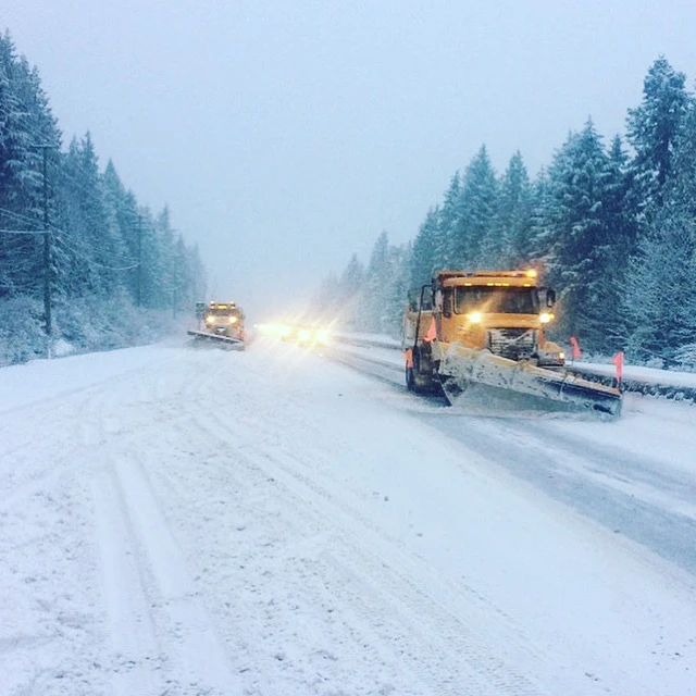two snowplows clear snow from a two-lane highway